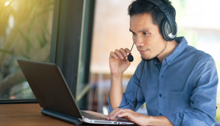 Person in a blue shirt using a laptop while wearing headphones.