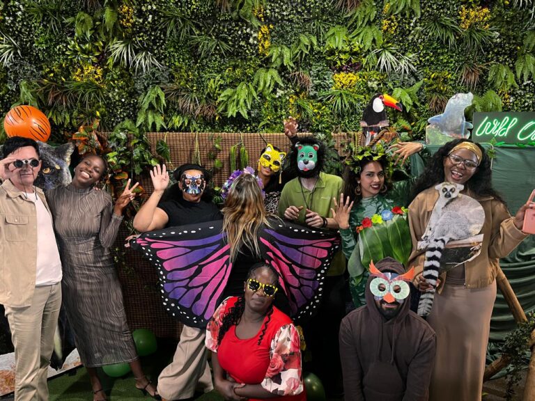 Group of people in costumes against a plant backdrop at a themed event.