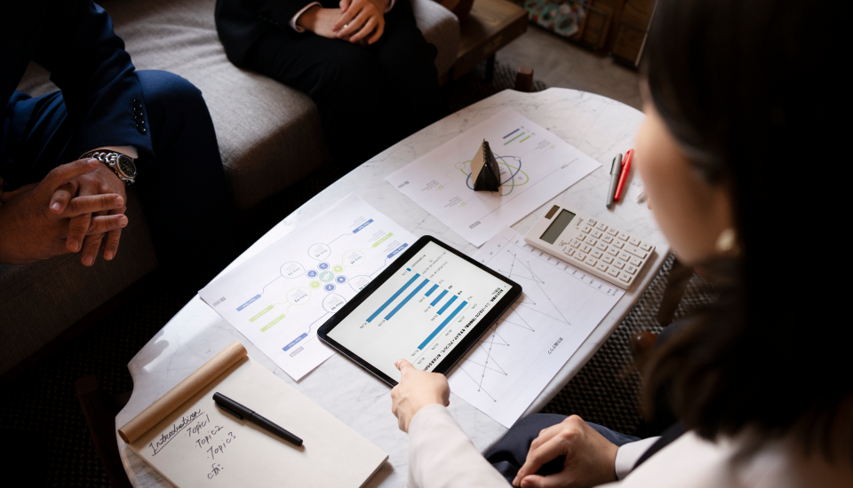 Professionals discussing charts on a tablet and papers during a meeting.