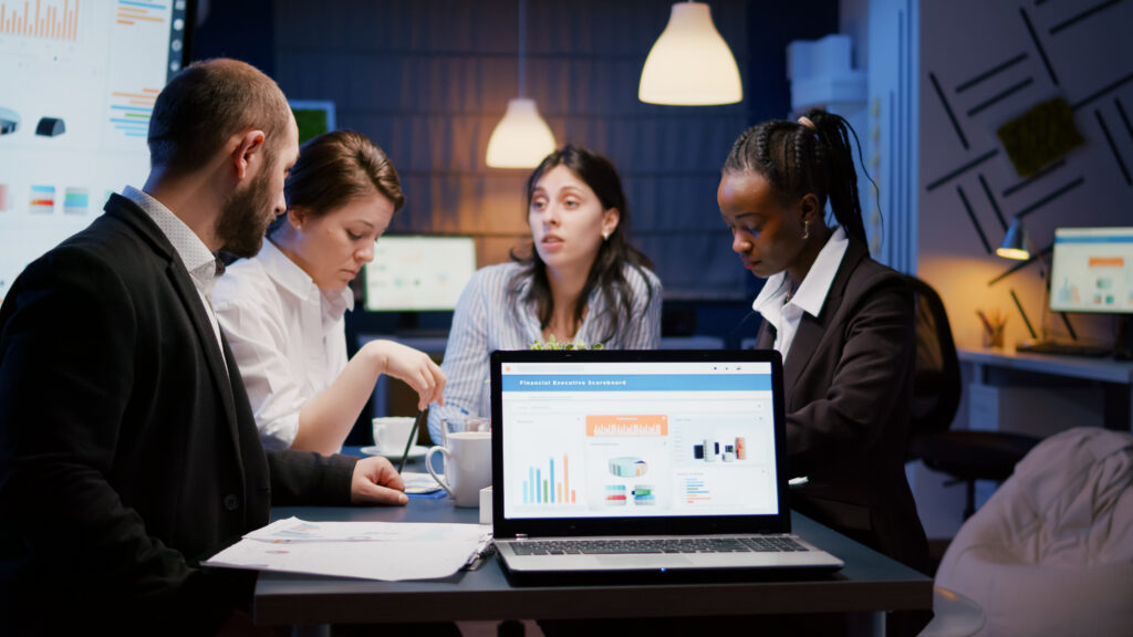 Team analyzing data on a laptop in a modern office at night.