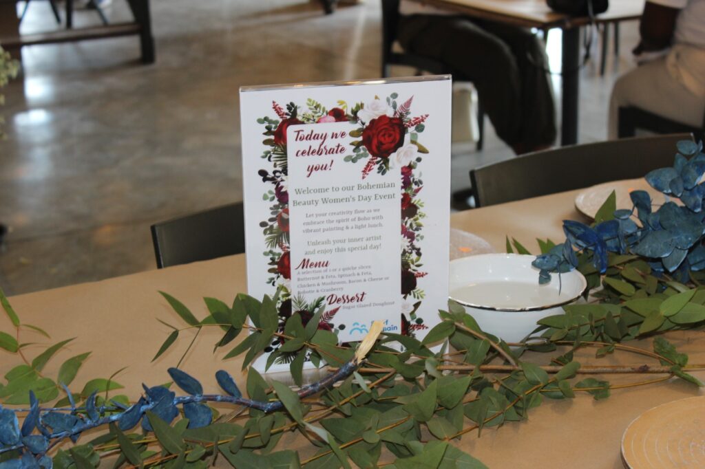 Event menu on a table with floral decoration and a blurred background of people sitting.