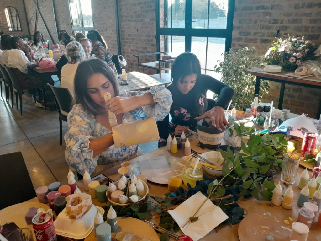 People sitting at a craft table with painting materials and greenery.