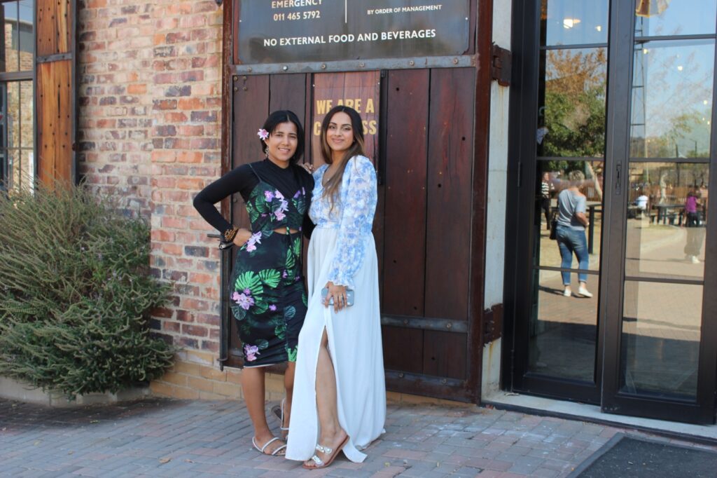 Two individuals in formal attire standing by a wooden door with a sign above.