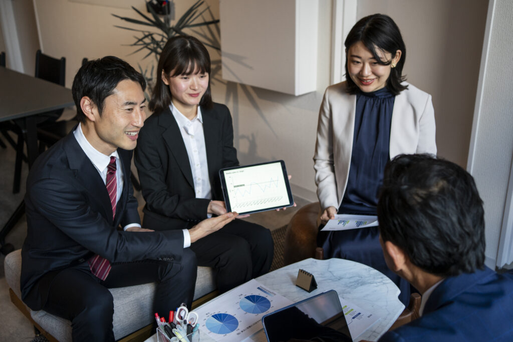 Three professionals in a meeting with documents and a digital tablet displaying graphs.