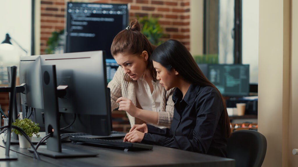 Two individuals working together at a computer in an office setting.