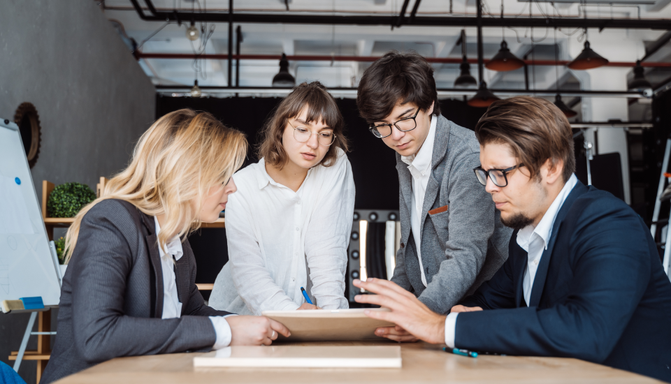 Four professionals collaborating around a table in a modern office setting.