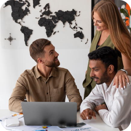 Three professionals with a laptop at a desk, a world map on the wall behind them.