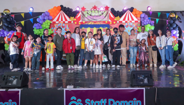 Group of people on a stage with carnival-themed decorations and balloons.